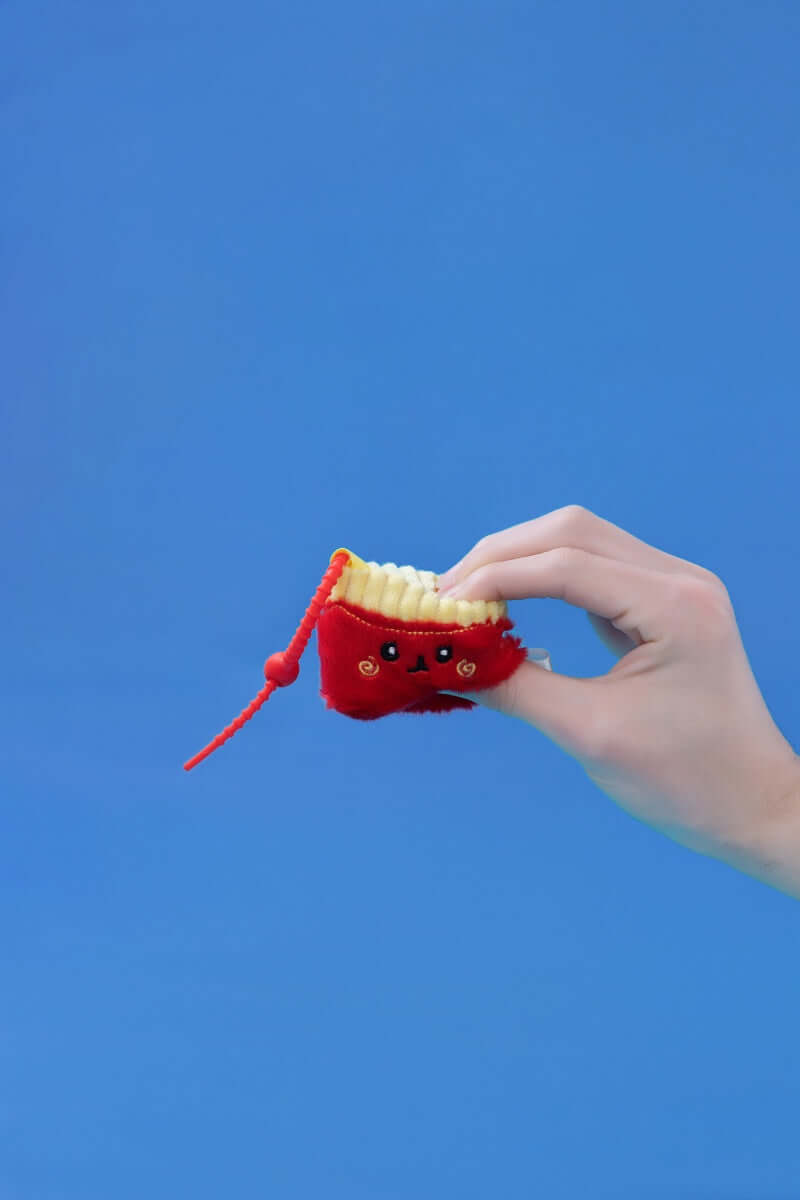 Hand holding a Mini Fries plush toy by Squarepals, featuring a cute design and durable clip strap.