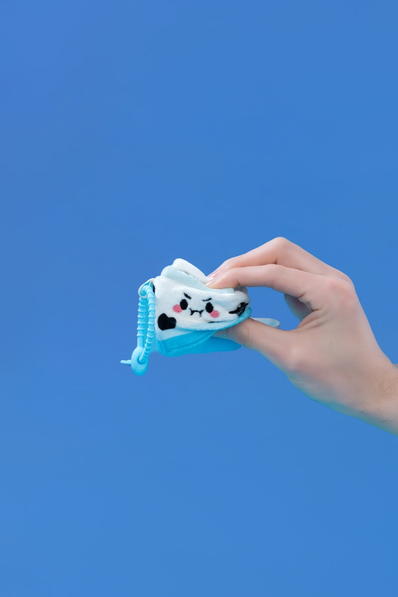 Mini Milk plush toy held in hand against a blue background, featuring a clip-on strap for easy attachment.