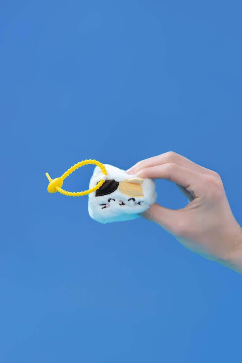 Mini Cat squishy plush toys held by a hand, featuring a yellow clip-on strap against a blue background.