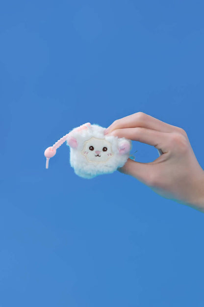 Mini squishy sheep plush toy held in hand against a blue background, showcasing its cute design and clip-on feature.
