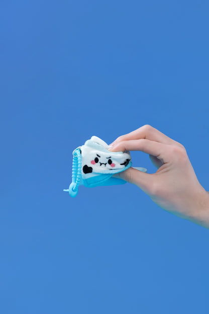 Mini Milk plush toy held in hand against a blue background, featuring a clip-on strap for easy attachment.